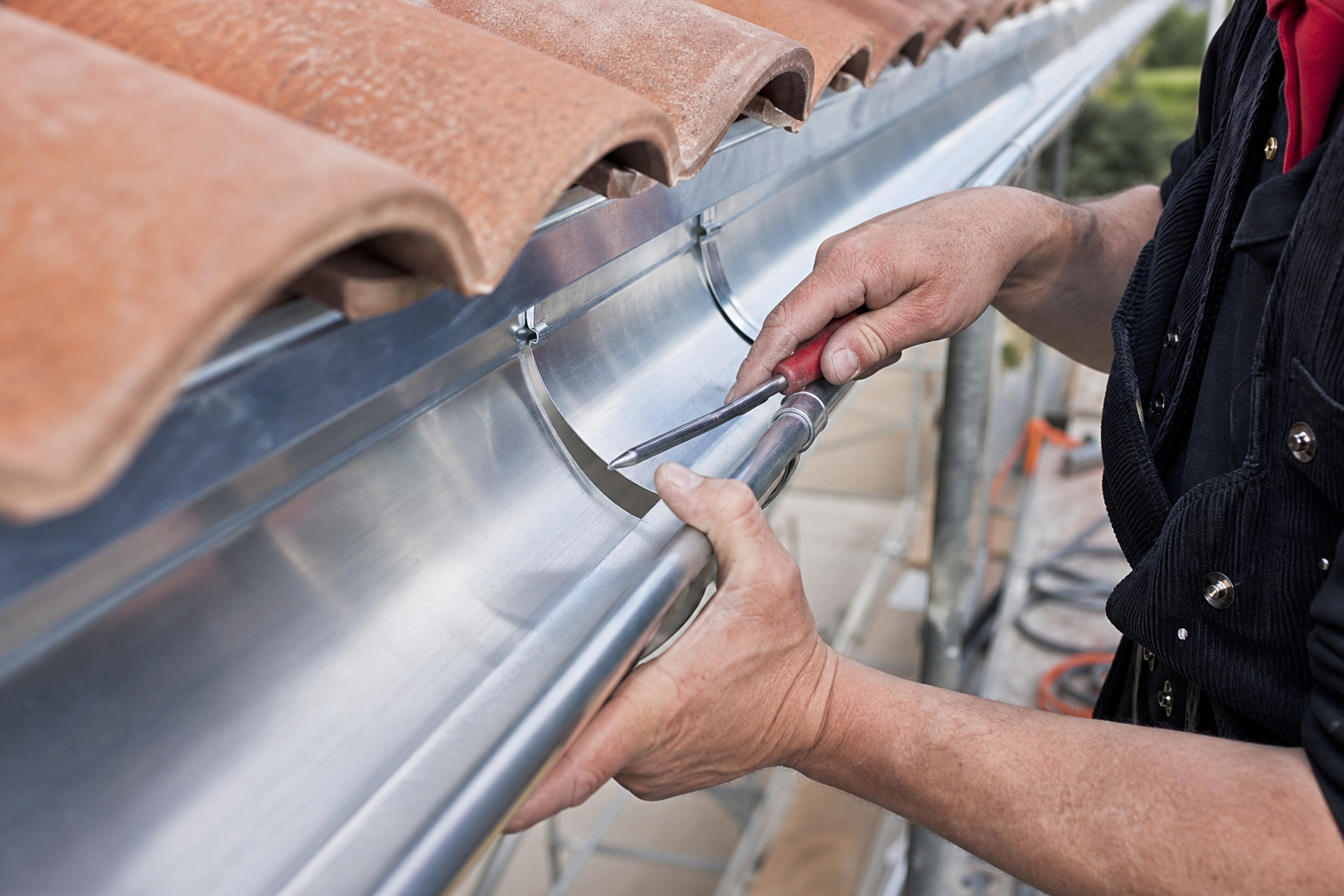 Installation de gouttière en zinc le long d'un toit en tuiles